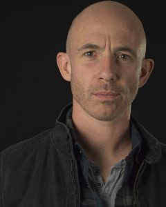Kevin Marron wearing dark jacket on dark background.