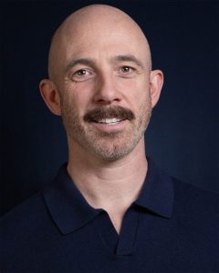 Kevin Marron with moustache on dark background.
